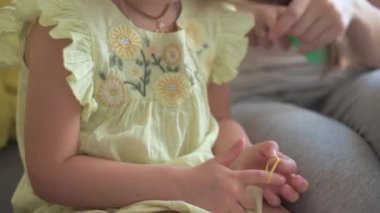 Otantik, genç, beyaz bir kadın annesi, çocuk örgüleriyle ilgileniyor sarı saçlı sarı saçlı kız örgüleri, gri kanepe üzerinde. Örgü örme işlemi. Moda ve güzellik, annelik kavramı.