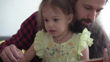 Rock tarzında mutlu bir adam, küçük çocukla rahat evinde gitar çalarak vakit geçirir. Baba küçük kızına müzik aleti çalmayı öğretir. Ev müziği dersinin keyfini çıkar. aile, eğitim, yaşam konsepti