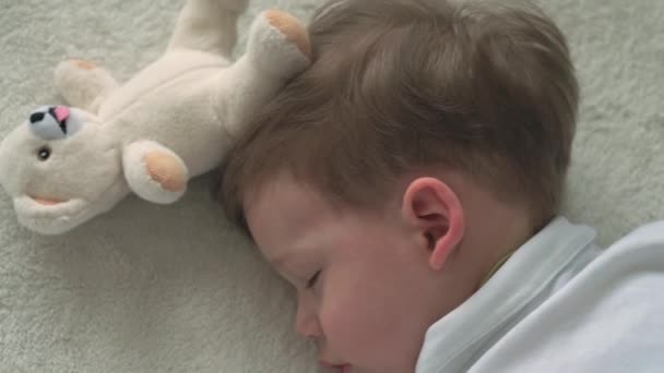 Автентичний крупним планом милий кавказький маленький дошкільний малюк хлопчик 2-3 роки солодко спить у зручному білому ліжку з плюшевим ведмедем. Догляд за дітьми, Спляча дитина, Дитинство, Батьківство, концепція життя — стокове відео