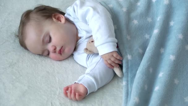 Автентичний крупним планом милий білий немовля пухнаста дівчинка спить солодко в зручному білому і синьому ліжку з плюшевим ведмедем. Догляд за дітьми, Спляча дитина, Дитинство, Батьківство, концепція життя — стокове відео