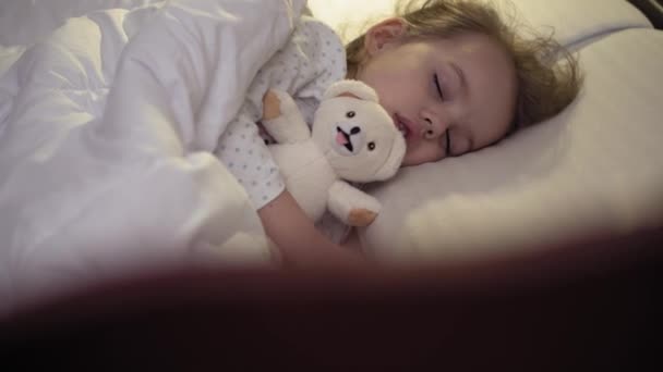 Аутентичный крупный план симпатичной кавказки, маленькая девочка дошкольного возраста 3-4 года спят сладко в удобной белой кровати с плюшевым медведем. Уход за детьми, Спящий ребенок, Детство, Родительство, концепция жизни — стоковое видео