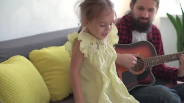 Rock tarzında mutlu bir adam, küçük çocukla rahat evinde gitar çalarak vakit geçirir. Baba küçük tatlı kız için şarkılar söyler müzik enstrümanı yerli müzik dersinin keyfini çıkar. aile, aşk, hayat konsepti — Stok video