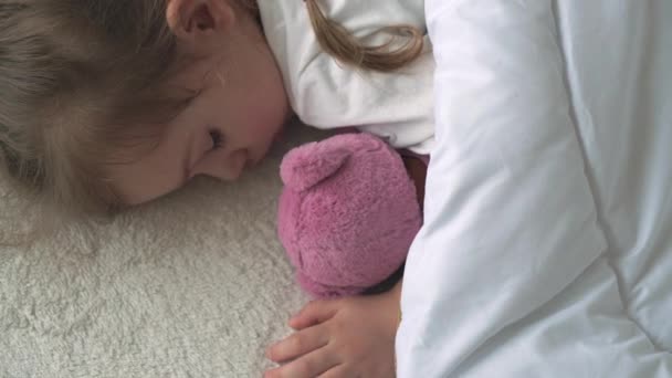 Authentische Nahaufnahme von niedlichen kaukasischen kleinen Vorschulkind Kind Mädchen 3-4 Jahre schlafen süß in bequemen weißen Bett mit Teddybär. Kinderbetreuung, Schlafendes Baby, Kindheit, Elternschaft, Lebenskonzept — Stockvideo