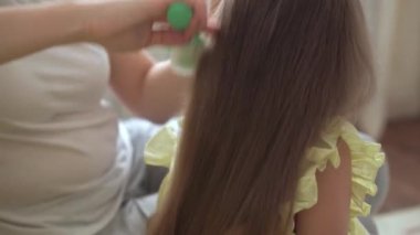 Otantik, genç, beyaz bir kadın annesi, çocuk örgüleriyle ilgileniyor sarı saçlı sarı saçlı kız örgüleri, gri kanepe üzerinde. Örgü örme işlemi. Moda ve güzellik, annelik kavramı.