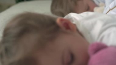 Anaokulunun şirin bebek şakalarının özgün yakın çekimi. Çocuklar ve kızlar oyuncak ayıyla rahat beyaz yatakta tatlı tatlı uyurlar. Çocuk bakımı, Uyuyan Bebek, Çocukluk, Ebeveynlik, Yaşam Konsepti.