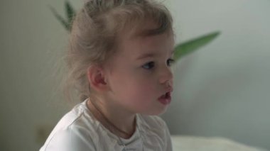 Beyaz yataktaki kameraya bakarak uyandığında çok uykulu olan beyaz, beyaz, küçük, şirin, beyaz bir anaokulu çocuğunun otantik yakın çekimi. Çocuk bakımı, Uyuyan Bebek, Çocukluk, Ebeveynlik, Yaşam Konsepti