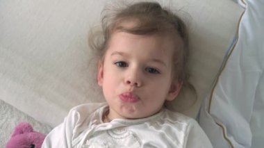 Beyaz yatakta kameraya bakan oyuncak ayıyla uyandığında küçük, şirin, beyaz bir anaokulu çocuğu uykulu bir şekilde kapanıyor. Çocuk bakımı, Uyuyan Bebek, Çocukluk, Ebeveynlik, Yaşam Konsepti