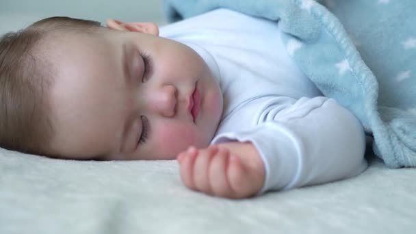 Автентична крупним планом мила біла маленька дитина пухнаста дівчинка солодко спить у зручному білому ліжку, покритому синьою ковдрою. Догляд за дітьми, Спляча дитина, Дитинство, Батьківство, концепція життя — стокове відео