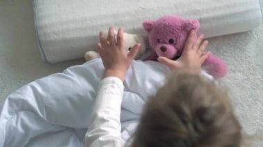 Otantik yakın plan şirin beyaz okul çocuğu küçük kız uykulu uyandığında oyuncak ayıcığı beyaz yatakta yatır. Çocuk bakımı, Uyuyan Bebek, Çocukluk, Ebeveynlik, Yaşam Konsepti