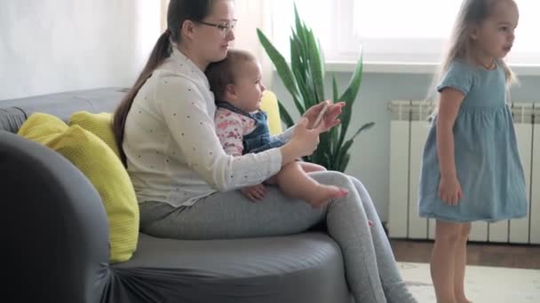 Kaukasiska familj små barn flicka pojke och mamma talar i videokonferens via smartphone tillsammans i vardagsrummet hemma med glädje leende. aktivitetsteknik livsstil mobiltelefon användning koncept — Stockvideo