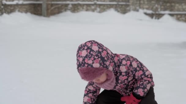 Zima, wakacje, gry, koncepcje rodzinne - środkowy plan autentycznego małego przedszkola małoletnia 3-4-letnia dziewczynka w fioletowym kolorze na zaśnieżonej łące bawi się śniegiem na wsi. dziecko biegnie po śnieżnej okolicy — Wideo stockowe
