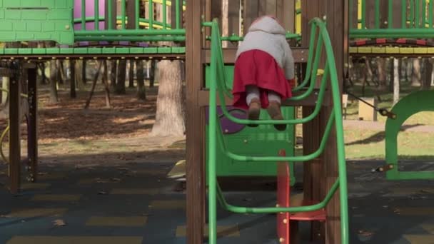 Infancia, familia, maternidad, concepto de actividades - niña preescolar menor de 2-4 años en boina naranja roja jugando en el patio de recreo en el frío parque de otoño. niño pequeño divertirse en escaleras pasos al aire libre — Vídeos de Stock