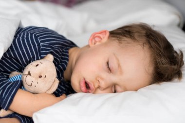 Otantik portre, beyaz yatakta oyuncak ayıyla uyuyan beyaz, beyaz, beyaz, beyaz, beyaz, beyaz, beyaz, beyaz, beyaz bir çocuk. Çocuk öğle yemeği vakti dinleniyor. bakım, ilaç ve sağlık, çocukluk, ebeveynlik, yaşam konsepti