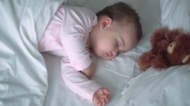 Otantik portre, beyaz yatakta oyuncak ayıyla pembe uykuda olan beyaz, beyaz, küçük, beyaz, tombul bir bebek bebek ya da oğlan. Çocuk öğle yemeği vakti dinleniyor. Bakım, Uyuyan Çocuk, Çocukluk, Ebeveynlik, Hayat Konsepti