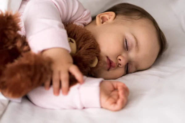 Authentiek portret schattig Kaukasisch klein baby mollig meisje of jongen in roze slaap met teddybeer op wit bed. kind rust uit rond lunchtijd. verzorging, Slaapkind, Jeugd, Ouderschap, levensloop — Stockfoto