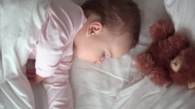 Otantik portre, beyaz yatakta oyuncak ayıyla pembe uykuda olan beyaz, beyaz, küçük, beyaz, tombul bir bebek bebek ya da oğlan. Çocuk öğle yemeği vakti dinleniyor. Bakım, Uyuyan Çocuk, Çocukluk, Ebeveynlik, Hayat Konsepti