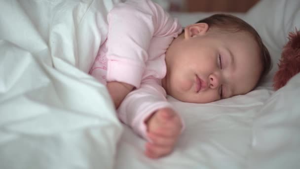 本物の肖像画かわいい白いベッドの上でテディベアとピンクの睡眠中のかわいい白人の小さな赤ちゃんぽっちゃりの女の子や男の子。お昼休みの子。ケア、睡眠の子供、子供、親、人生の概念 — ストック動画