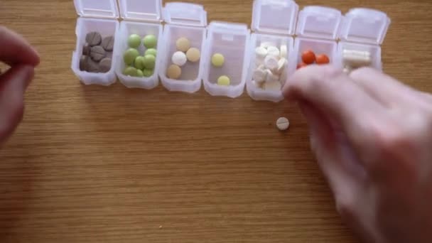 Close-up van mannelijke hand vingers sorteren gekleurde pillen in stapels op plastic organisator doos. zieke man op zoek naar genezing in medicatie planner. Traditionele en alternatieve geneeskunde en gezondheid, covid-19 concept — Stockvideo