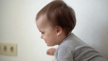 Göğsünde haç olan otantik bebek tombul kız garip bir şekilde yürüyor ve sürünüyor. Küçük çocuk tek başına eğitim oyunları oynuyor. Oyun odasında yürümeyi öğreniyor. Çocukluk, aile, yalıtım konsepti