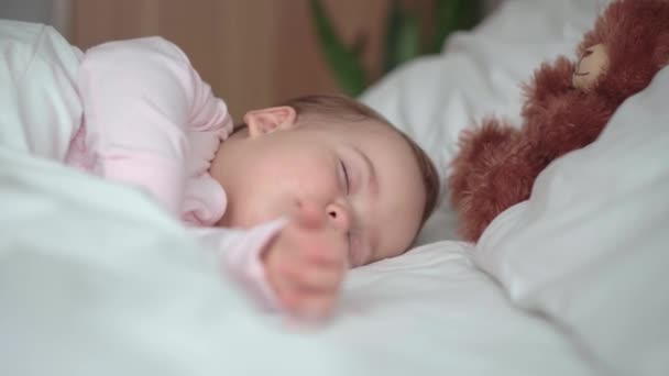 Auténtico retrato lindo bebé caucásico regordete niña o niño en sueño rosa con oso de peluche en la cama blanca. niño descansando a la hora del almuerzo. cuidado, Niñez durmiente, Infancia, paternidad, concepto de vida — Vídeo de stock