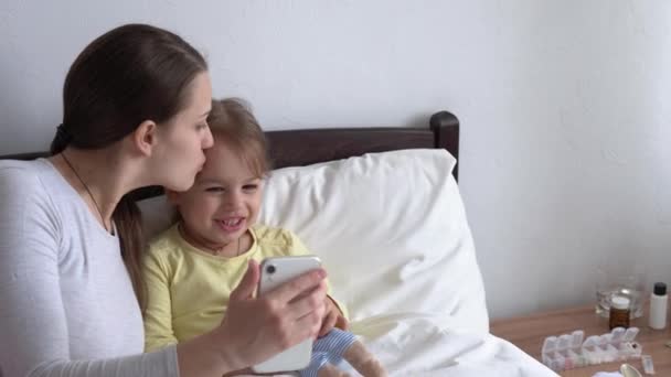 Kaukasische familie kleine kinderen meisje en jonge vrouw moeder praten in video conferentie door smartphone samen thuis met geluk glimlach op wit bed. technologie, levensstijl, concept van mobiel telefoongebruik — Stockvideo