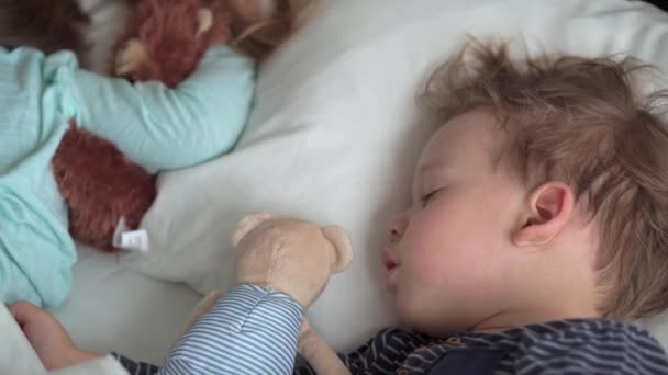 Authentisches Porträt niedlichen kaukasischen kleinen Vorschulgeschwistern Baby Junge und Mädchen im blauen Schlaf mit Teddybär auf weißem Bett. Mittags ruhen die Kinder. Pflege, Medizin und Gesundheit, Kindheit, Lebenskonzept — Stockvideo