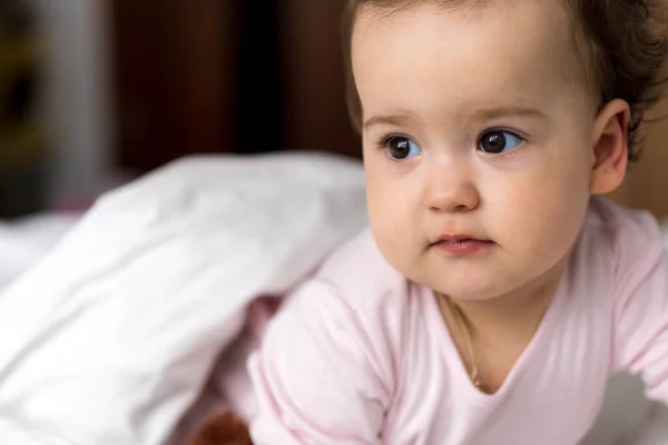 Retrato autêntico bonito caucasiano pequeno bebê gordinho menina ou menino em rosa sonolento ao acordar olhando para a câmera na cama branca. Cuidados infantis, Infância, Paternidade, conceito de estilo de vida — Fotografia de Stock