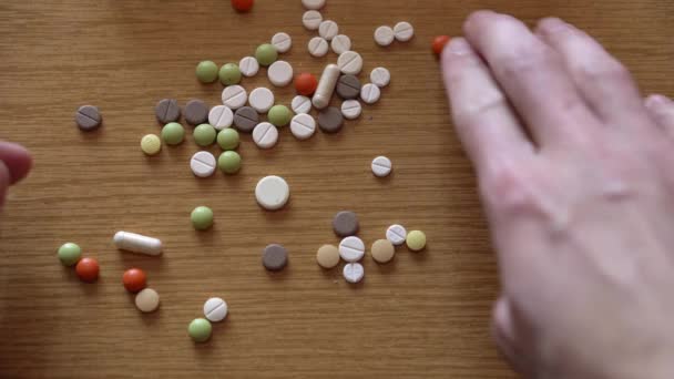 A férfi kezek extrém közelsége a színes tablettákat egy halomba rendezi a fa asztalon. Beteg ember, aki gyógymódot keres a gyógyszertervezőben. Hagyományos és alternatív gyógyászat és egészség, covid-19 koncepció — Stock videók