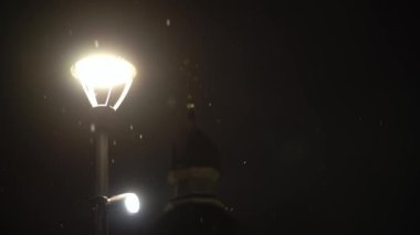 Gece parkındaki parlak ışık fenerinin üzerindeki kar yağışı kış öncesi çekim için harika. Akşam şehir manzarası. Meteoroloji, Hava Durumu, Doğal Fenomen, Mutlu Noeller ve Yeni Yıl Konsepti