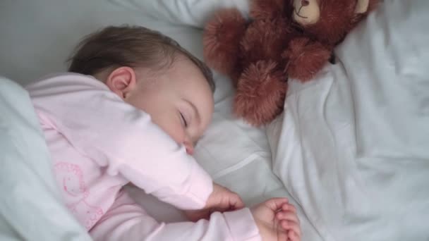 Authentisches Porträt niedlichen kaukasischen kleinen Säugling pummelig Baby Mädchen oder Junge im rosa Schlaf mit Teddybär auf weißem Bett. Mittags ruhen die Kinder. Pflege, Schlafkind, Kindheit, Elternschaft, Lebenskonzept — Stockvideo