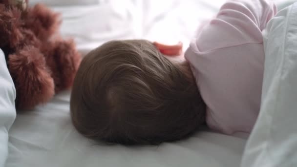 Auténtico retrato lindo bebé caucásico regordete niña o niño en sueño rosa con oso de peluche en la cama blanca. niño descansando a la hora del almuerzo. cuidado, Niñez durmiente, Infancia, paternidad, concepto de vida — Vídeo de stock