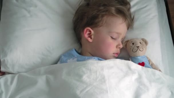 Authentisch süße kaukasische kleine Vorschulgeschwister Baby Junge und Mädchen in blau rosa Pyjama schlafen mit Teddybär auf weißem Bett. Kindererholung, Pflege, Medizin und Gesundheit, Kindheit, Lebenskonzept — Stockvideo