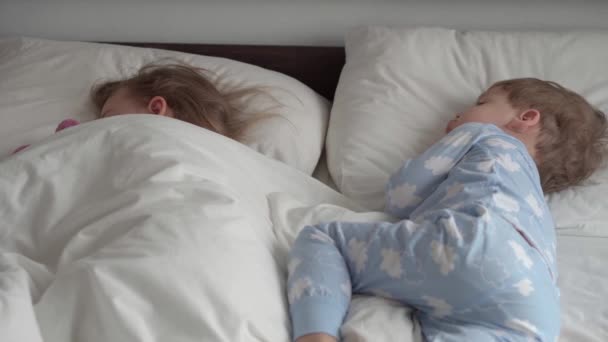 本物の肖像画2かわいい白人の小さな就学前の兄弟赤ちゃんの男の子と女の子は白いベッドの上でテディベアで青いピンクのパジャマ睡眠で。子供の休息、ケア、医療、健康、子供時代、人生の概念 — ストック動画