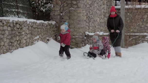 Vacaciones, juego, concepto de familia slo-mo auténtico tres niños preescolares felices hermanos con la madre joven trineo y jugar con la nieve. nevadas en temporada fría en invierno patio al aire libre — Vídeos de Stock