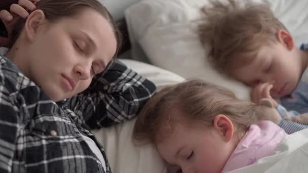 Authentieke schattige jonge moeder viel in slaap lees sprookje van boek tot baby voor het slapen gaan. vrouw zorgt voor slapende kinderen. Twee kinderen slapen in een wit bed. Moederdag, moederschap, kinderconcept — Stockvideo