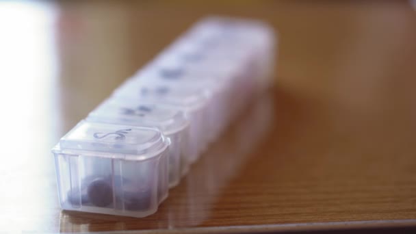 Heroriëntering van dicht bij de afstand van plastic organisator doos voor pillen met cellen gemarkeerd zwarte marker op dagen van de week. Traditionele en alternatieve geneeskunde en gezondheid, ziekte, pandemie, covid-19 concept — Stockvideo