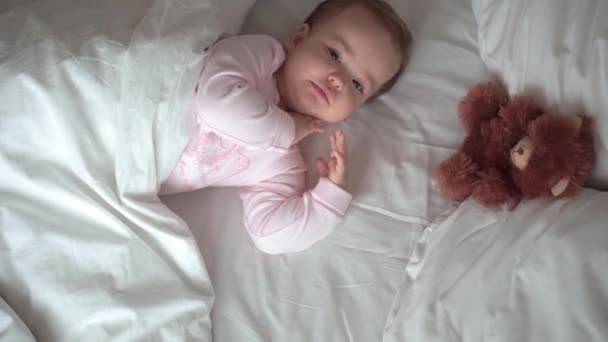 Authentisches Porträt niedlichen kaukasischen kleinen Säugling pummelig Baby Mädchen oder Junge im rosa Schlaf mit Teddybär auf weißem Bett. Mittags ruhen die Kinder. Pflege, Schlafkind, Kindheit, Elternschaft, Lebenskonzept — Stockvideo