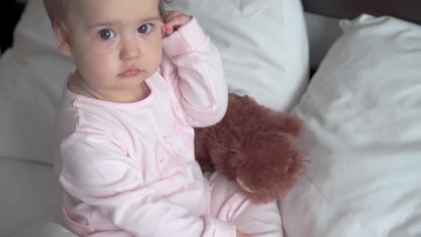 Äkta porträtt kaukasiskt litet spädbarn knubbig liten flicka eller pojke i rosa sömnig när du vaknar tittar på kameran ler söta och grimaser i vit säng. Barnomsorg, Barndom, Föräldraskap, Livskoncept — Stockvideo