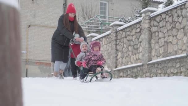 Διακοπές, παιχνίδι, οικογενειακή έννοια - slo-mo αυθεντικό τρία ευτυχισμένα παιδιά προσχολικής ηλικίας αδέλφια με μικρά wonan μαμά έλκηθρο και να παίξει με το χιόνι. χιονόπτωση σε κρύο καιρό εποχής σε εξωτερικούς χώρους χειμερινής αυλής — Αρχείο Βίντεο