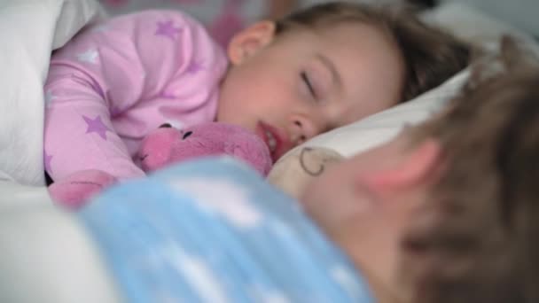 Authentiek portret schattige blanke kleine kleuter broers en zussen baby jongen en meisje in blauw roze pyjama slapen met teddybeer op wit bed. Kinderrust, verzorging, geneeskunde en gezondheid, Kindertijd, levensconcept — Stockvideo