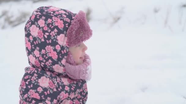 Wakacje, gra, koncepcja dzieciństwa - slo-mo autentyczne szczęśliwe przedszkola maluch dziewczynka uśmiech patrząc na aparat i jeść płatki śniegu i śniegu z dłoni. opady śniegu w okresie zimowym Pogoda w zimie na zewnątrz — Wideo stockowe