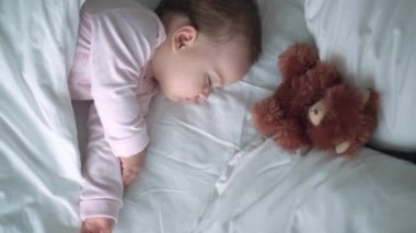 Otantik portre, beyaz yatakta oyuncak ayıyla pembe uykuda olan beyaz, beyaz, küçük, beyaz, tombul bir bebek bebek ya da oğlan. Çocuk öğle yemeği vakti dinleniyor. Bakım, Uyuyan Çocuk, Çocukluk, Ebeveynlik, Hayat Konsepti