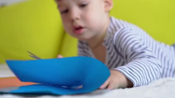 オンライン学習アート教育- 1つの創造的な就学前、幼児の少年は、テーブルの上にはさみのシチンで色の紙を切り出す工芸品を作る。小さな幸せな子供が家で隔離され手の動きが — ストック動画