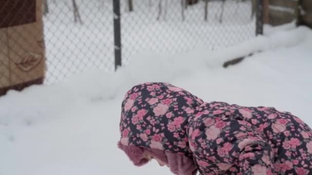 L'hiver, les vacances, les jeux, les concepts familiaux - le plan moyen de la petite fille authentique maternelle mineure de 3-4 ans en violet sur la prairie enneigée joue avec la neige dans la campagne. enfant court sur une zone enneigée — Video