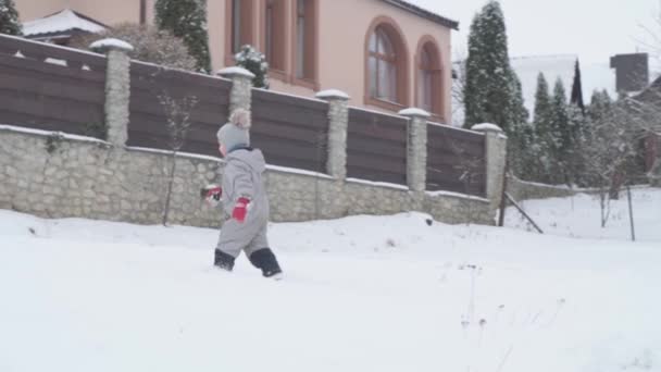 Wakacje, dzieciństwo, gra, koncepcja rodziny - slo-mo autentyczne Jeden szczęśliwy przedszkolak dziecko chłopiec w ciepłym szarym kapeluszu uruchomić na śnieżnej drodze. opady śniegu w zimną pogodę w parku zimowym na zewnątrz w pobliżu domu — Wideo stockowe