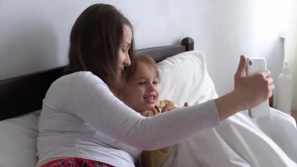 Kaukasische familie kleine kinderen meisje en jonge vrouw moeder praten in video conferentie door smartphone samen thuis met geluk glimlach op wit bed. technologie, levensstijl, concept van mobiel telefoongebruik — Stockvideo