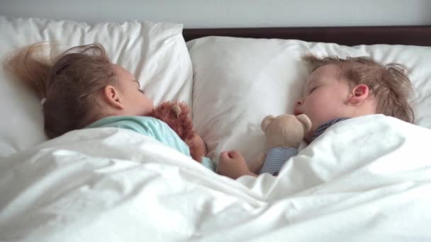 Authentic portrait cute caucasian little preschool siblings baby boy and girl in blue sleep with teddy bear on white bed. child resting at lunchtime. care, medicine and health, Childhood, life concept — Stock Video