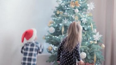 2 otantik mutlu Joy çocukları el sallıyor ve Noel ağacı oyunuyla neşeleniyorlar. Birlikte iyi eğlenceler. Anaokulundaki küçük çocuklar evde yeni yılı kutluyorlar. Kış, tatil, aile kavramı