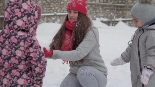 Xo@-@ mo authentique mignon heureux jeune femme maman en chapeau rouge avec des enfants prendre la neige avec les mains vomir sur la tête sourire. chutes de neige dans le parc d'hiver à l'extérieur. maternité, fête des mères, vacances, concept familial — Video