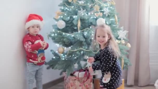 3 niños felices auténticos alegría saludar de la mano regocijarse por el juego del árbol de Navidad divertirse juntos. Los niños preescolares celebran el ambiente festivo de Año Nuevo en casa. Invierno, vacaciones, concepto familiar — Vídeo de stock